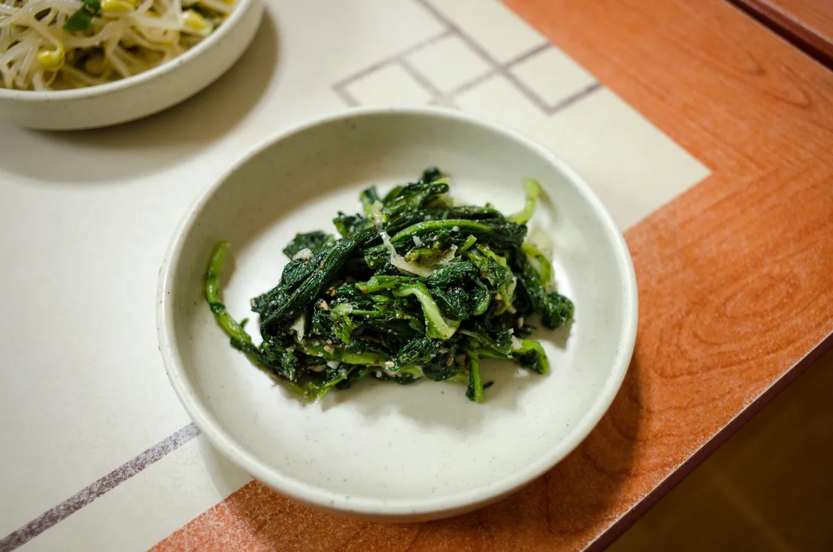 A small white bowl of seasoned spinach namul on a restaurant table