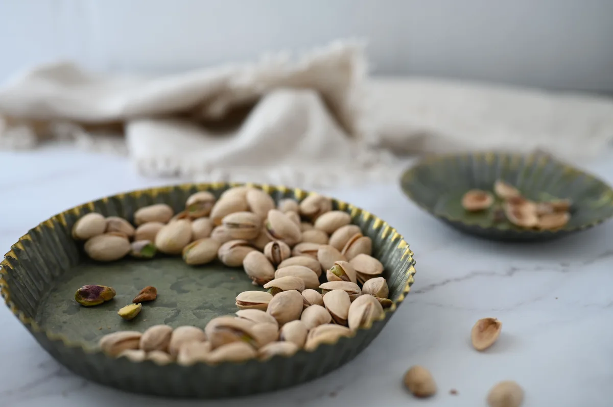 A shallow green dish of pistachios in their shells on a marble counter