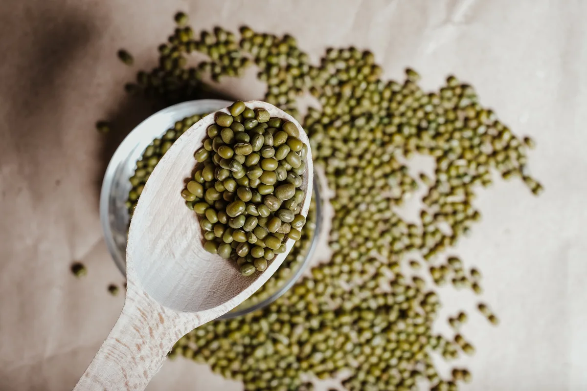 A wooden scoop of whole mung beans over a scattering of more beans
