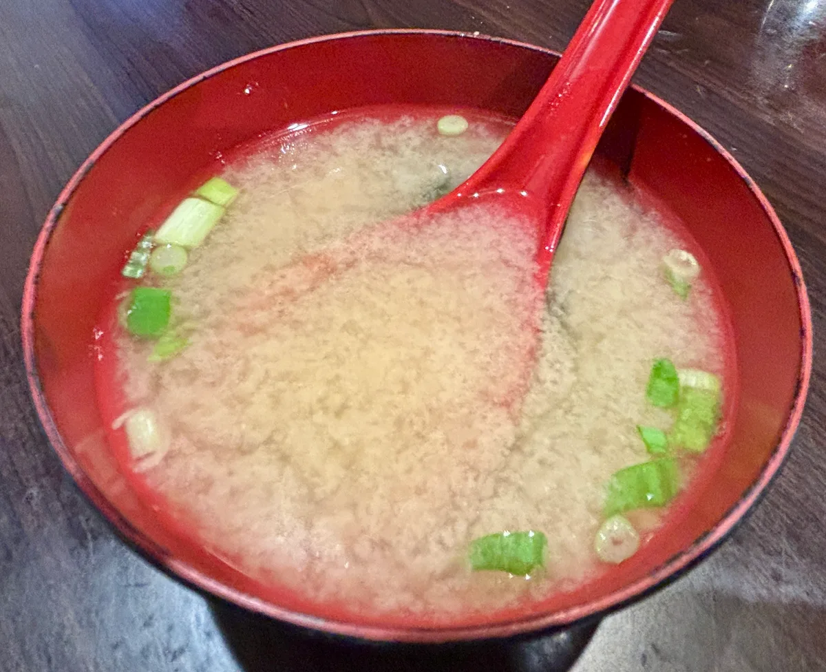 A red lacquer bowl of plain miso soup with sliced scallions