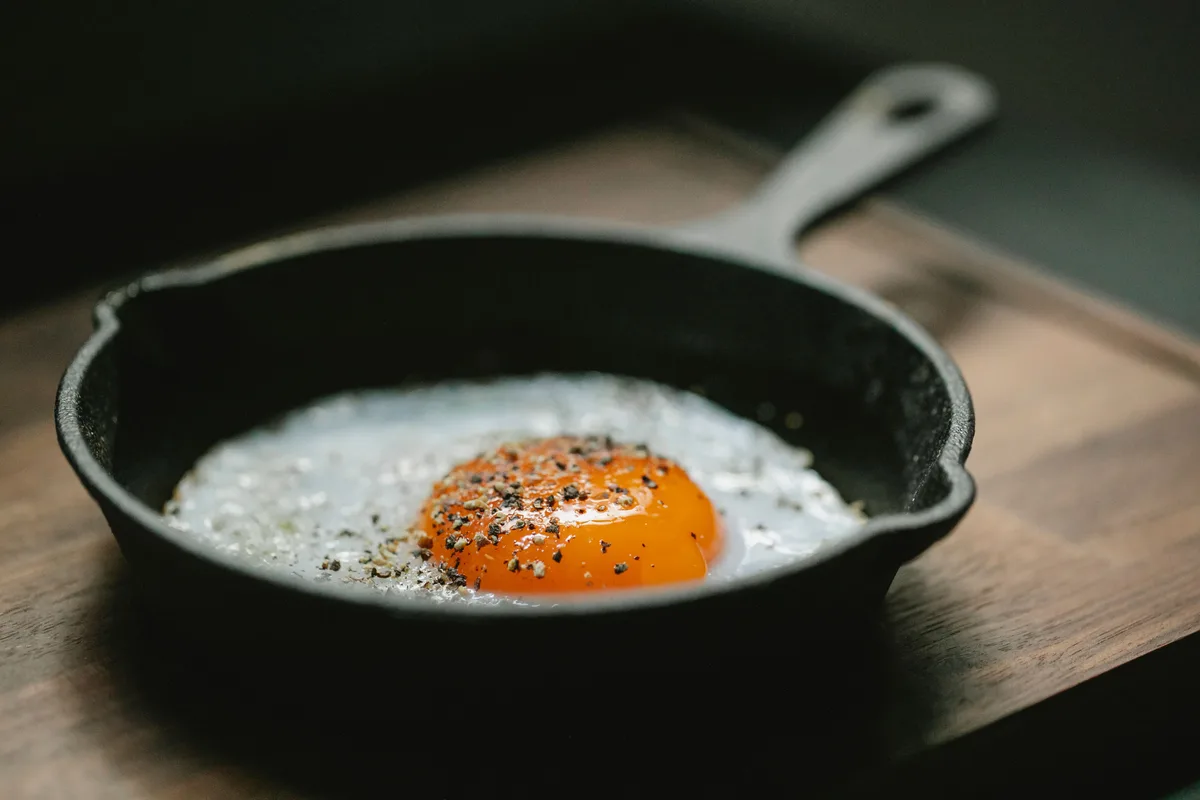 A fried egg sprinkled with black pepper in a small cast-iron skillet