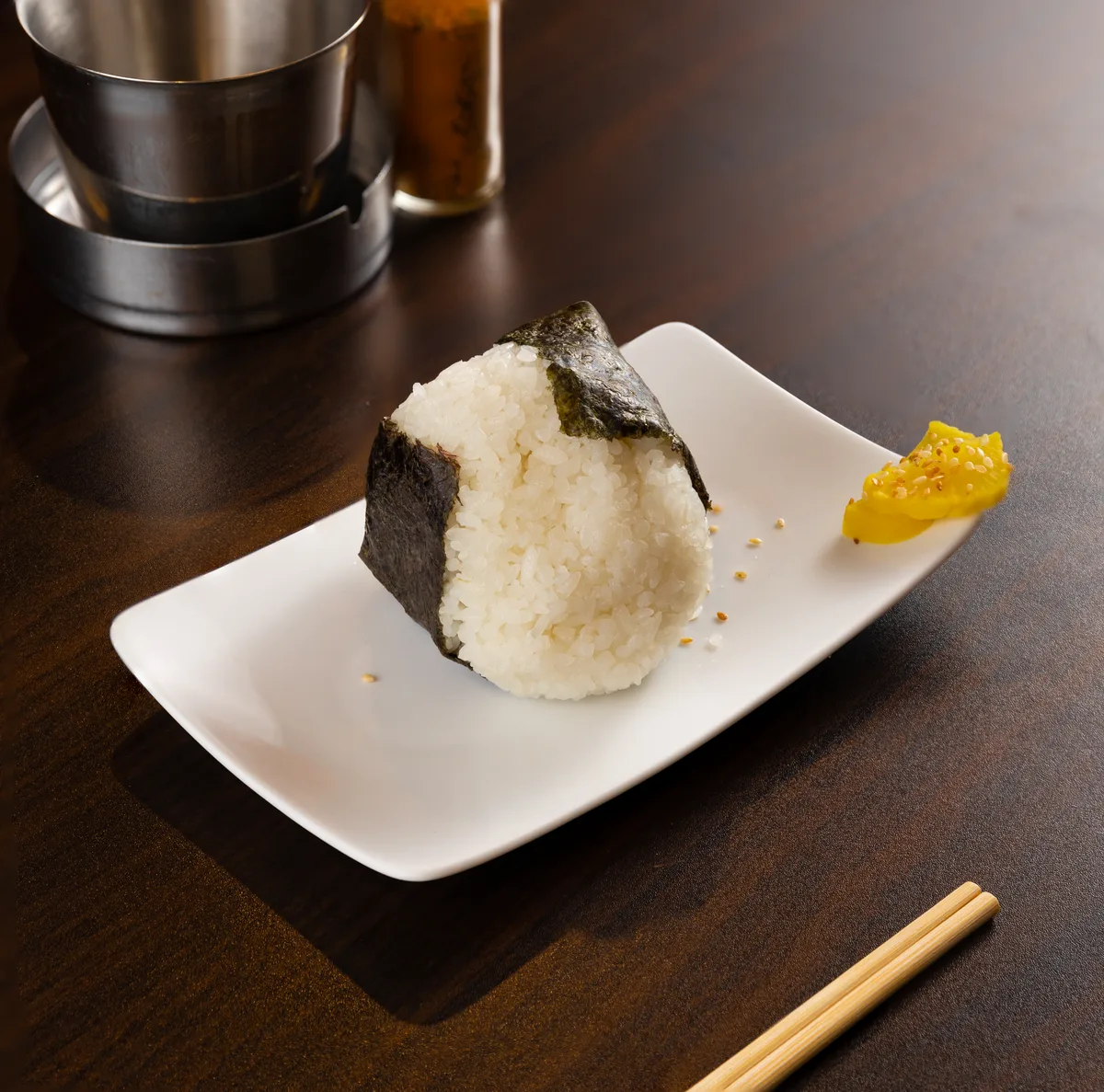 A rice ball wrapped in nori on a white plate, its short grains pressed together but still distinct