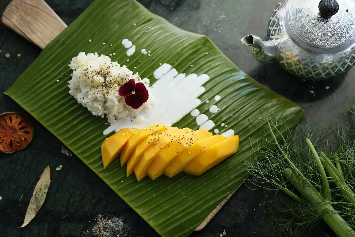 Mango sticky rice on a banana leaf, with coconut cream poured over the rice