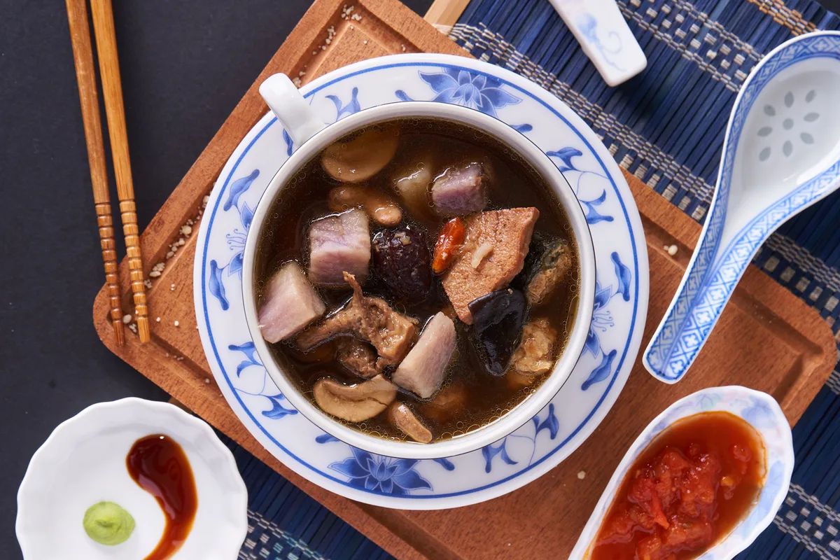 A dark Chinese soup with mushrooms in a blue-and-white porcelain bowl, with chopsticks and a spoon on the side