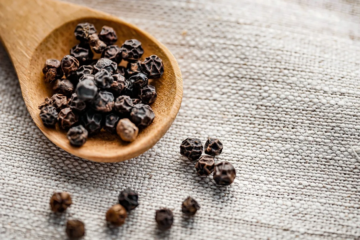 Black peppercorns in a wooden spoon on a linen cloth
