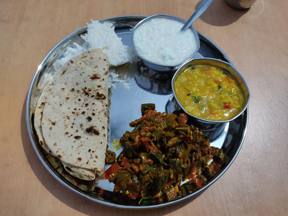 A steel thali with chapati, okra, yellow dal, rice and a small bowl of raita